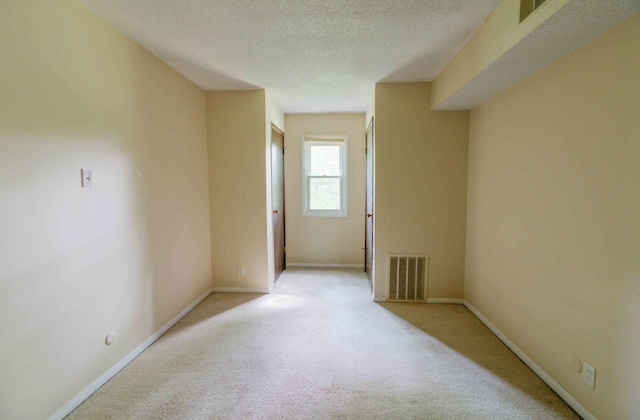 empty room with light colored carpet and a textured ceiling