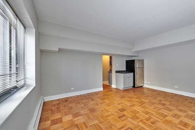 basement featuring a baseboard radiator, light parquet flooring, and stainless steel fridge