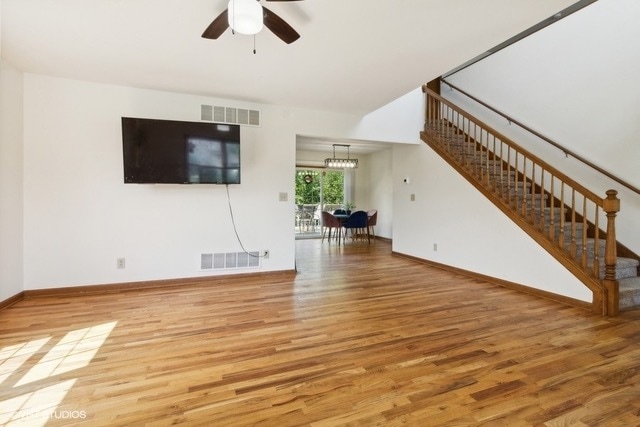 unfurnished living room featuring ceiling fan with notable chandelier and light wood-type flooring