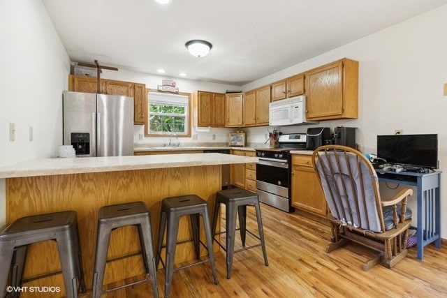 kitchen featuring appliances with stainless steel finishes, a kitchen bar, kitchen peninsula, and light wood-type flooring