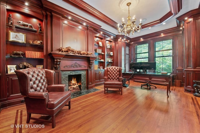 office space featuring built in shelves, crown molding, a fireplace, a notable chandelier, and wood finished floors