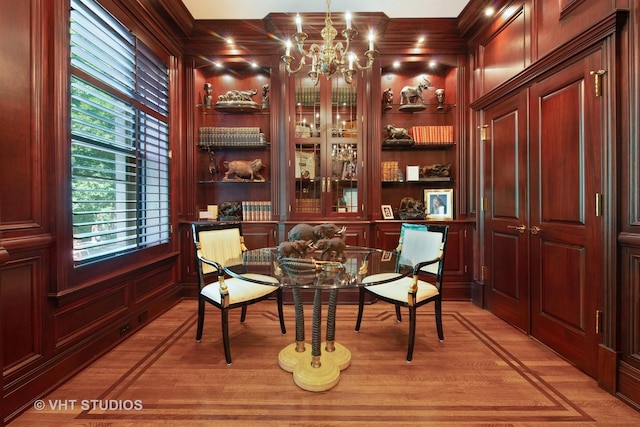 sitting room featuring built in features, light wood-type flooring, wood walls, and an inviting chandelier