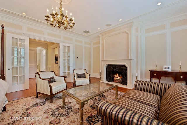 living area with arched walkways, a decorative wall, ornamental molding, a high end fireplace, and wood finished floors