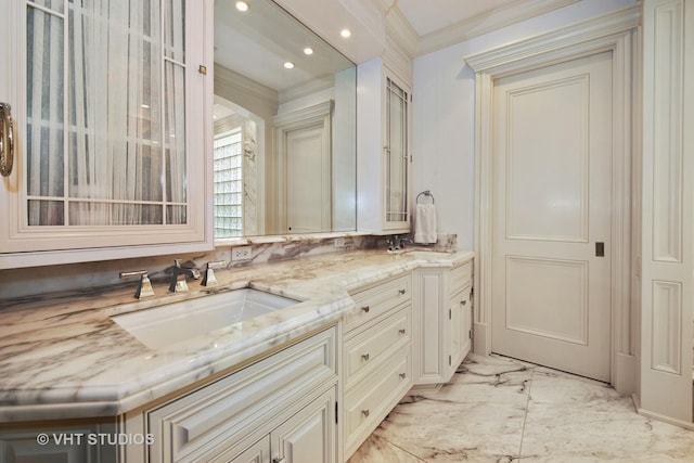 full bath with double vanity, marble finish floor, ornamental molding, and a sink