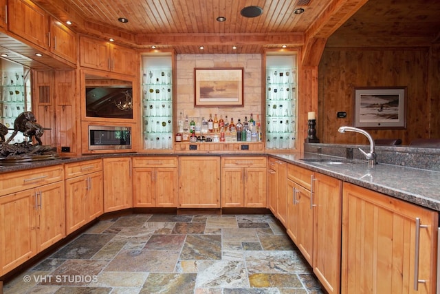 kitchen featuring dark stone counters, wood ceiling, stainless steel microwave, stone finish flooring, and a sink