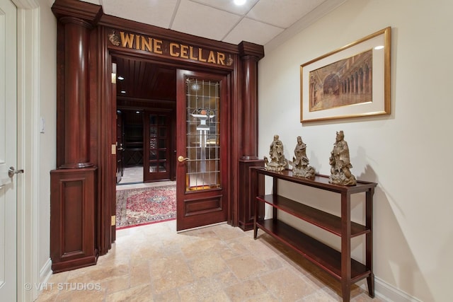 entrance foyer with a paneled ceiling, ornate columns, stone finish floor, and baseboards