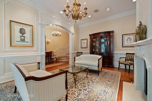 living area featuring arched walkways, a chandelier, a decorative wall, ornamental molding, and decorative columns