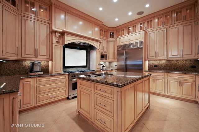 kitchen featuring premium appliances, light tile patterned flooring, a sink, dark stone counters, and a center island with sink