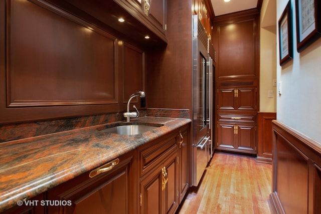 kitchen featuring light stone counters, crown molding, light wood-style floors, wainscoting, and a sink