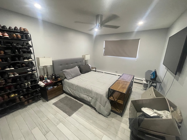 bedroom with ceiling fan, light wood-type flooring, and a baseboard heating unit