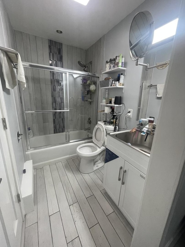 bathroom featuring wood finished floors, enclosed tub / shower combo, vanity, and toilet