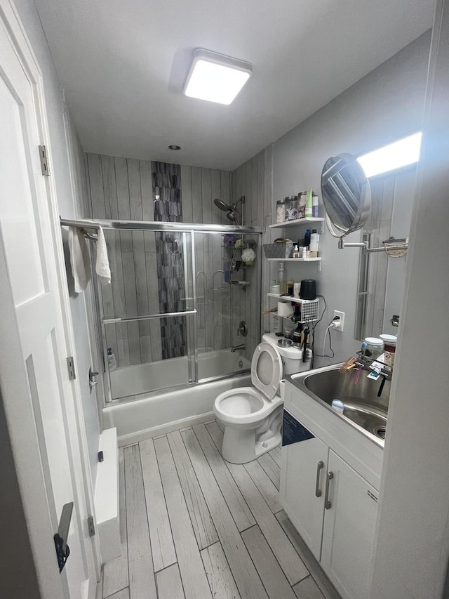 full bath with wood finished floors, bath / shower combo with glass door, vanity, and toilet