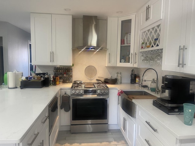 kitchen with stainless steel gas stove, wall chimney range hood, a sink, white cabinetry, and recessed lighting