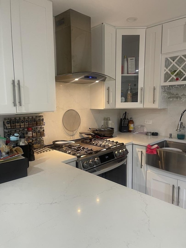 kitchen featuring wall chimney range hood, stainless steel range with gas cooktop, a sink, and white cabinetry