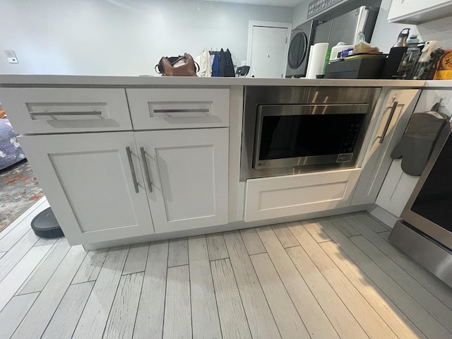 kitchen view of light wood finished floors, stainless steel microwave, white cabinets, and washer / dryer