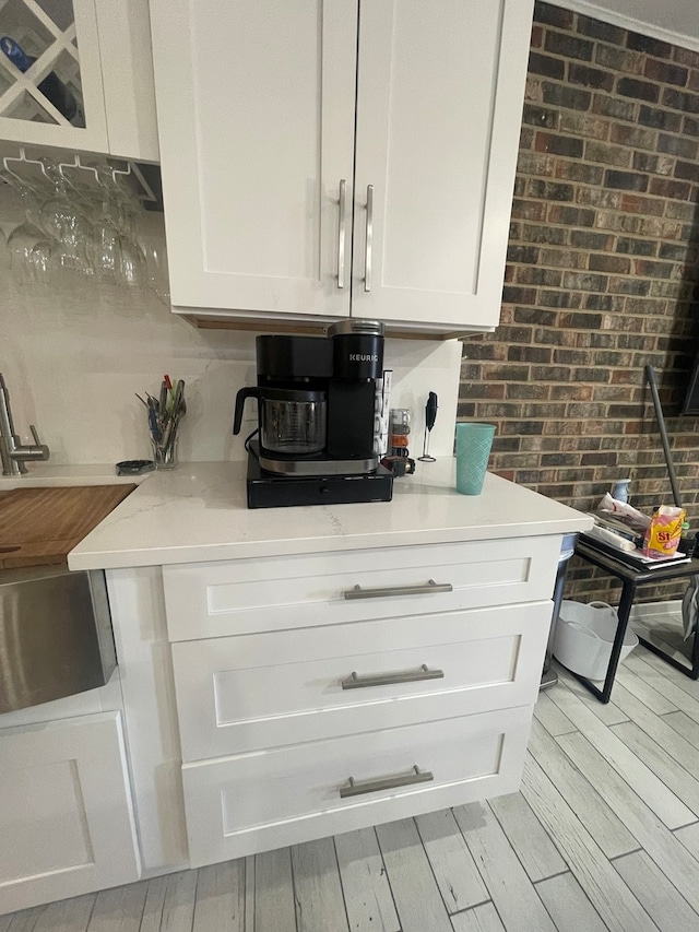 kitchen featuring white cabinetry, light hardwood / wood-style floors, brick wall, and light stone counters