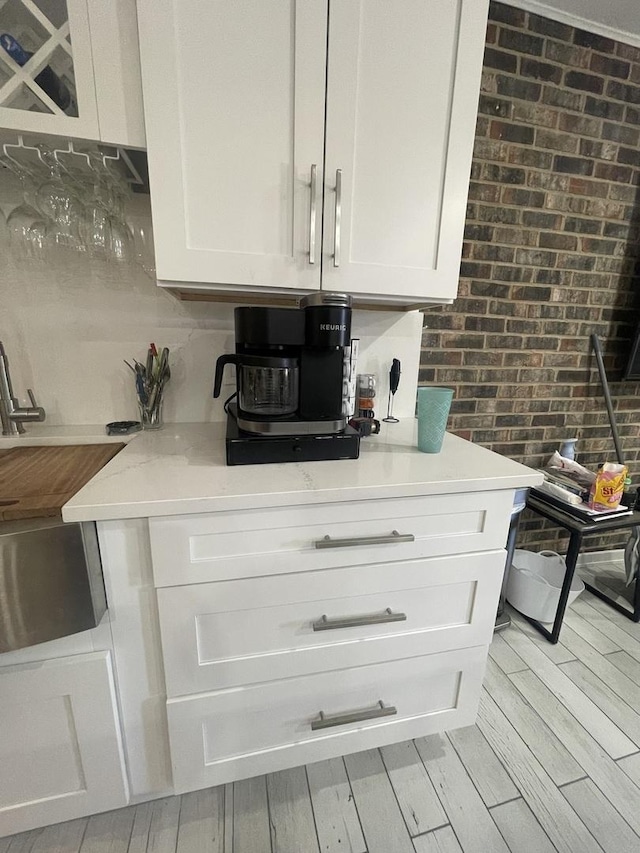 kitchen with light wood finished floors, white cabinetry, and brick wall