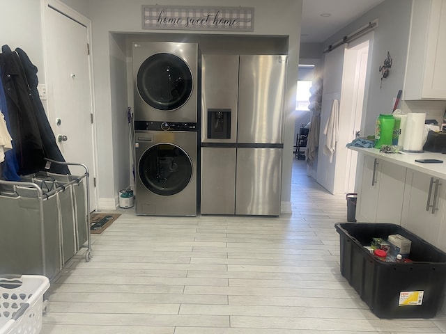 clothes washing area featuring a barn door, light hardwood / wood-style floors, and stacked washer and clothes dryer