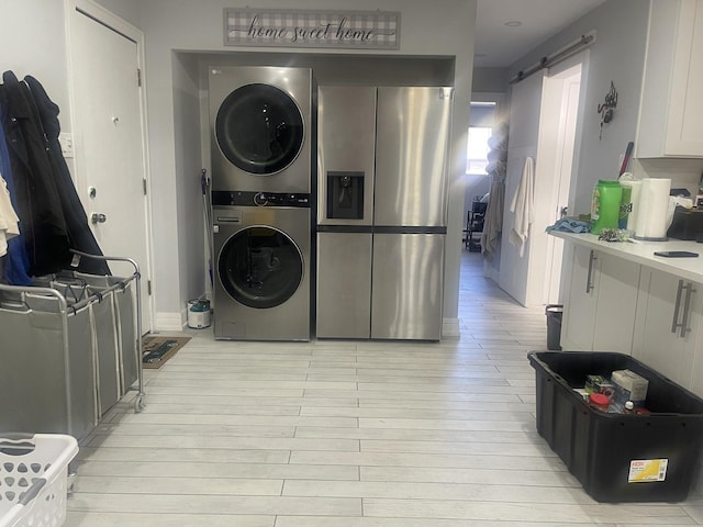clothes washing area featuring stacked washer / dryer, a barn door, and light wood-style floors