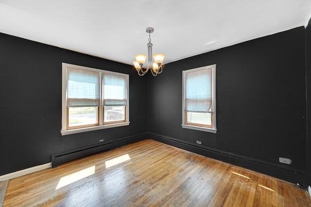 empty room featuring an inviting chandelier, baseboard heating, and light wood-type flooring