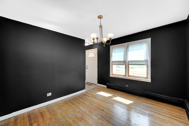 empty room with baseboard heating, light wood-type flooring, and a chandelier