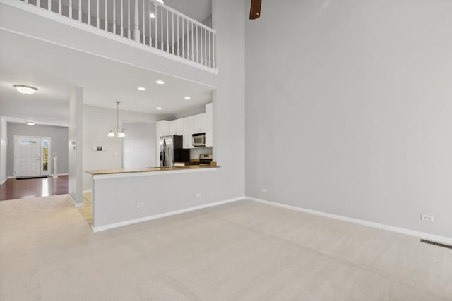 unfurnished living room with a notable chandelier, a high ceiling, and light carpet