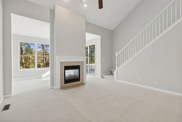 unfurnished living room with a tiled fireplace, light carpet, vaulted ceiling, and ceiling fan