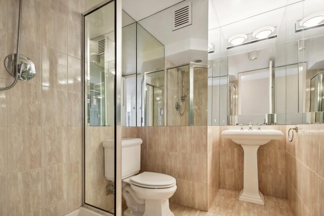 bathroom with tile patterned floors, an enclosed shower, tile walls, and toilet