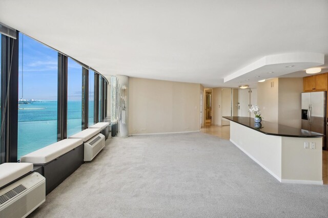 unfurnished living room with expansive windows, a water view, and light carpet