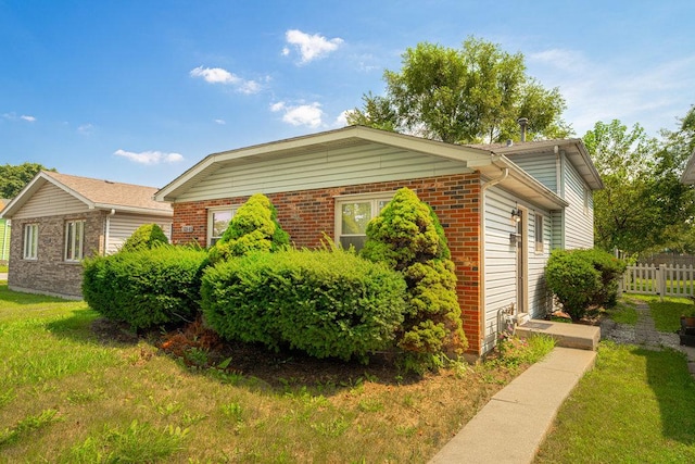 view of side of home with brick siding, fence, and a lawn