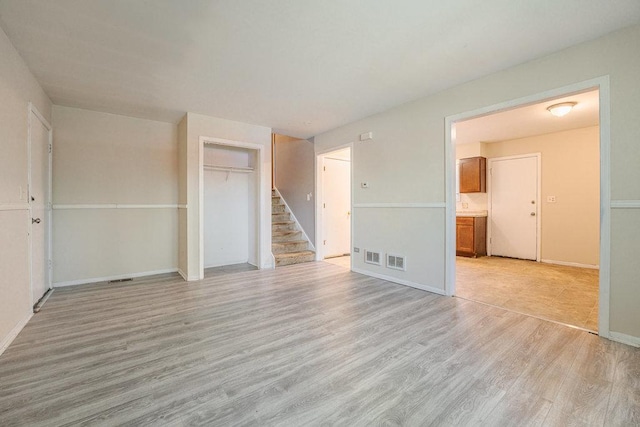 interior space featuring stairway, light wood-type flooring, visible vents, and baseboards