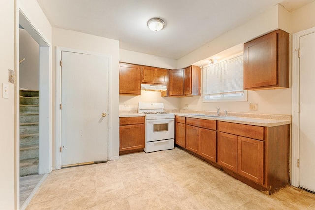 kitchen featuring under cabinet range hood, brown cabinets, a sink, and white gas stove