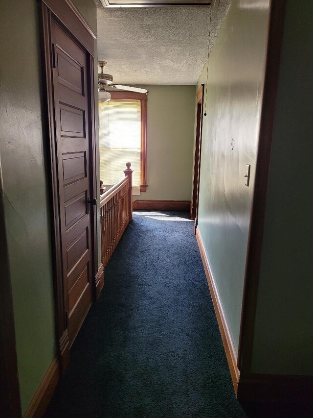 corridor with dark carpet and a textured ceiling