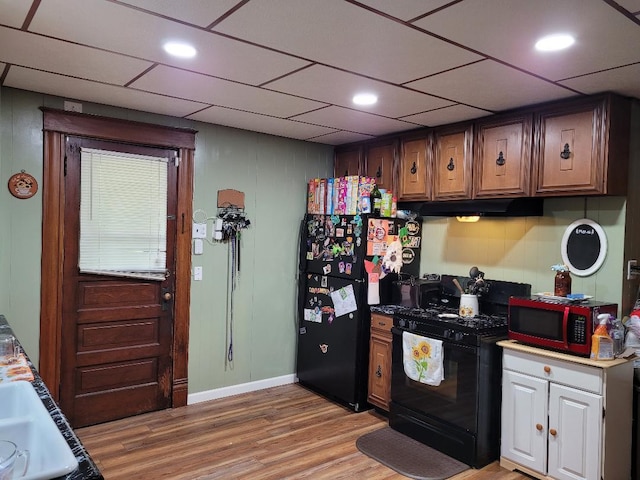 kitchen with dark brown cabinets, a drop ceiling, black appliances, and light hardwood / wood-style floors