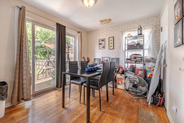 dining space featuring brick wall, hardwood / wood-style flooring, and baseboards