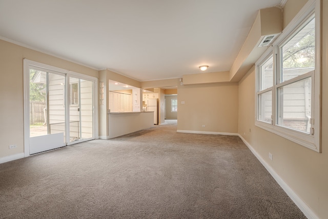 unfurnished living room with a wealth of natural light, light carpet, and crown molding