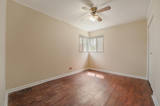 spare room with dark wood finished floors, visible vents, a ceiling fan, ornamental molding, and baseboards