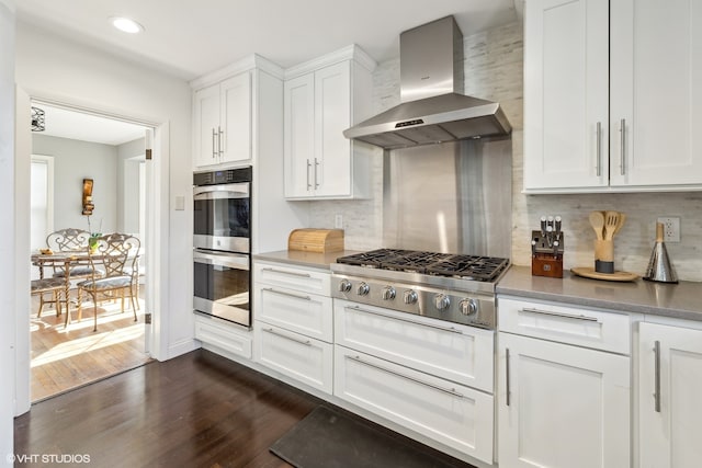 kitchen with stainless steel appliances, white cabinets, backsplash, dark hardwood / wood-style flooring, and wall chimney exhaust hood