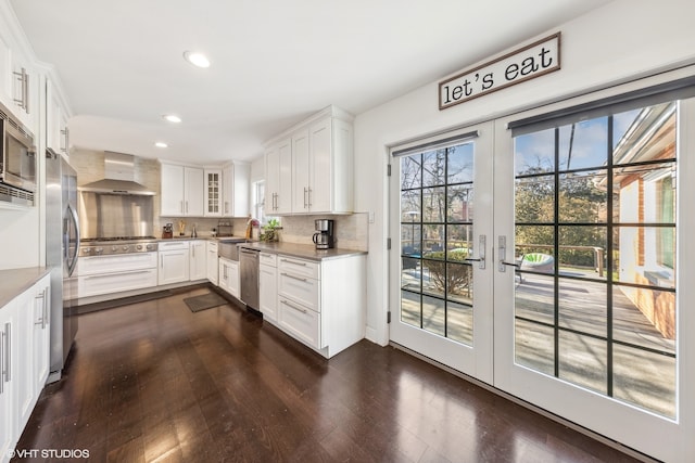 kitchen featuring wall chimney range hood, french doors, dark hardwood / wood-style floors, appliances with stainless steel finishes, and backsplash