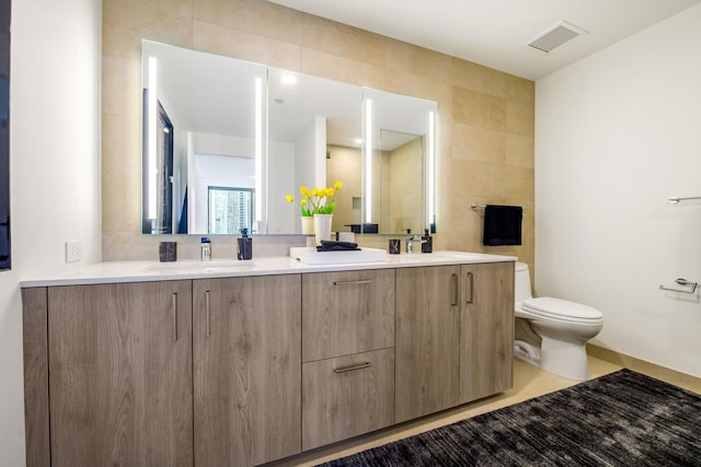 bathroom featuring tile walls, toilet, visible vents, a sink, and double vanity