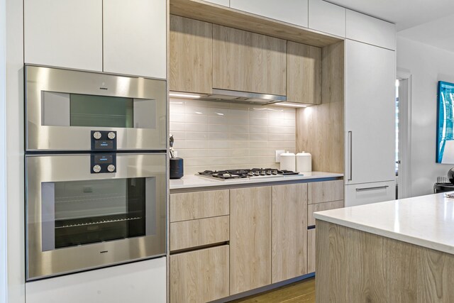 kitchen with light brown cabinetry, appliances with stainless steel finishes, light stone counters, wood-type flooring, and decorative backsplash