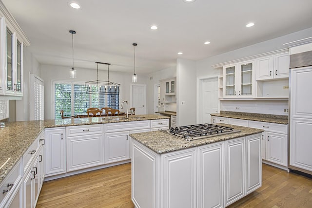 kitchen featuring a kitchen island, decorative light fixtures, stainless steel gas stovetop, sink, and white cabinets