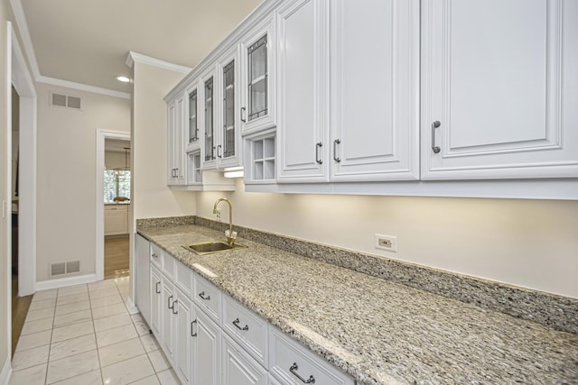 kitchen with sink, light tile patterned floors, white cabinetry, ornamental molding, and light stone countertops