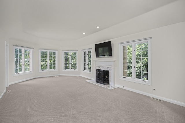 unfurnished living room with light carpet, a tray ceiling, and a high end fireplace