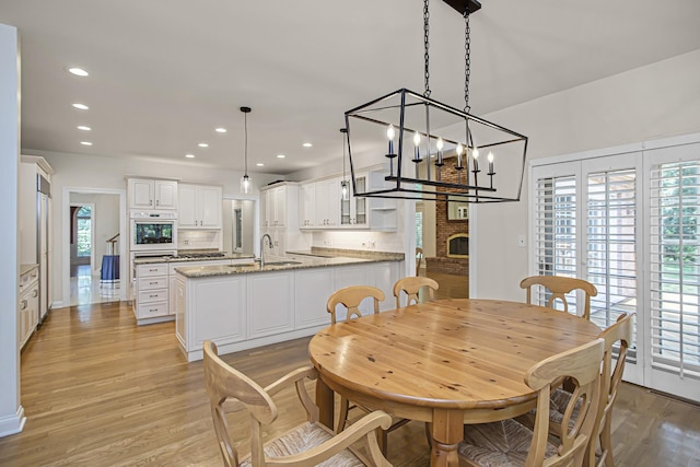 dining room with a brick fireplace, sink, and light wood-type flooring