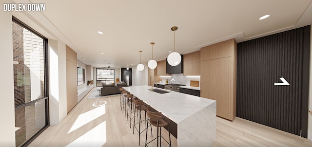 kitchen featuring an island with sink, a breakfast bar, sink, light stone counters, and light wood-type flooring