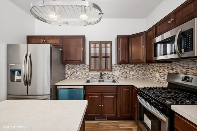 kitchen featuring appliances with stainless steel finishes, sink, decorative backsplash, dark brown cabinetry, and light hardwood / wood-style floors