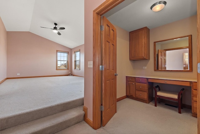 office area with ceiling fan, built in desk, vaulted ceiling, and light carpet