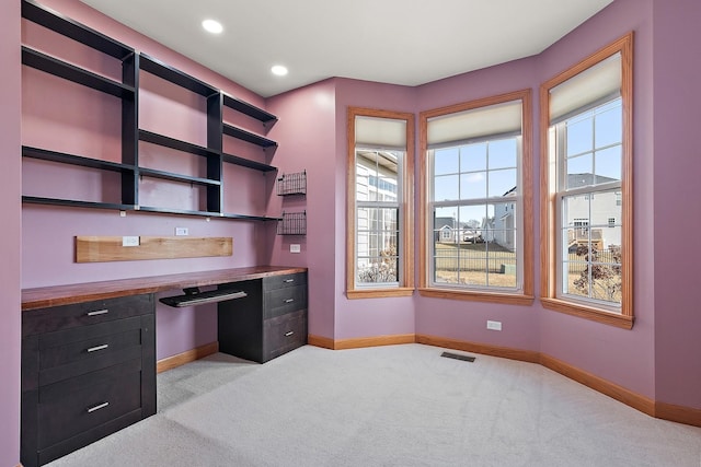 unfurnished office with light carpet, a healthy amount of sunlight, and built in desk