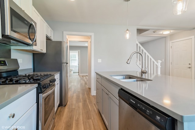 kitchen with light hardwood / wood-style flooring, appliances with stainless steel finishes, sink, pendant lighting, and a kitchen island with sink